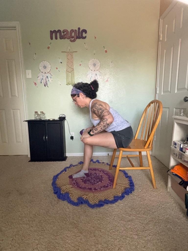 Girl sitting on chair with left ankle over right thigh and leaning forward.